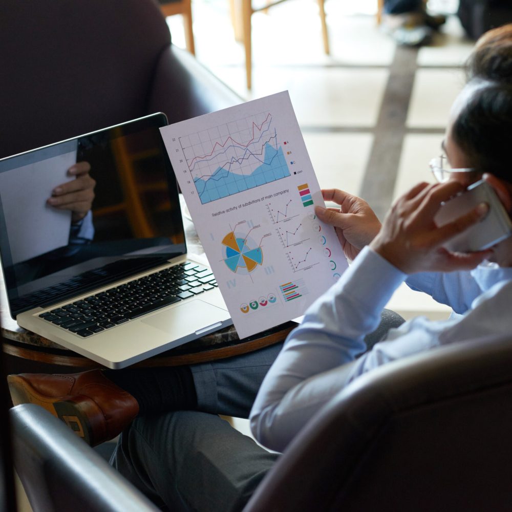 Businessman analyzing financial report in his hand and calling on the phone, view over the shoulder